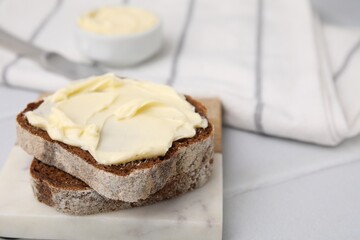 Slices of tasty bread with butter on white tiled table, closeup. Space for text