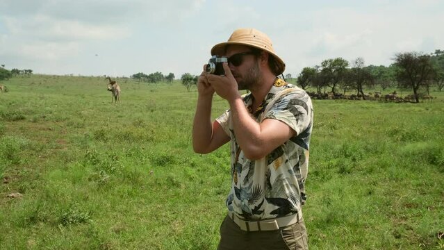 male tourist traveler with camera traveling on safari with giraffes in Africa. a large herd of giraffes in the savannah eating grass. a man in safari clothes takes photographs of wild animals