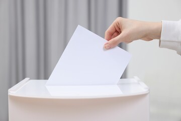 Woman putting her vote into ballot box on blurred background, closeup