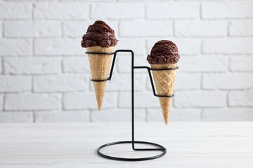 Chocolate ice cream scoops in wafer cones on white wooden table against brick wall