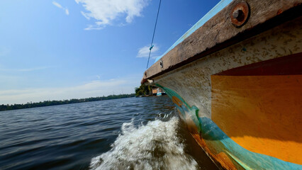 Fishing boat in the river, first person view. Action. Old boat floating along green shore and blue...