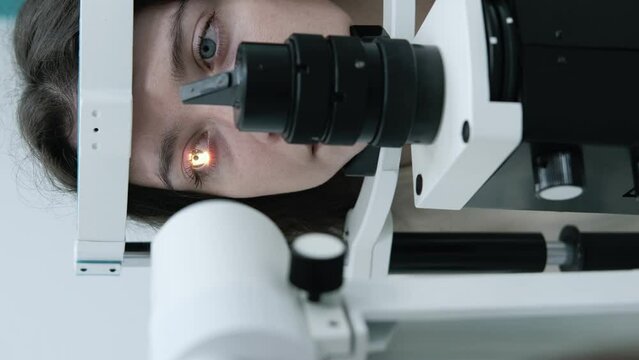 Attentive optometrist examining beautiful female patient with slit lamp in ophthalmology clinic. Optometrist during an examination in a modern clinic. Eyesight check. Front view
