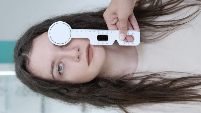Attentive optometrist examining a beautiful female patient, testing her vision using a ruler to determine interpupillary distance with an occluder in an ophthalmology clinic. Examination in a clinic
