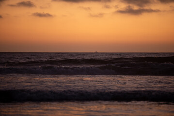 Fototapeta premium waves crash in pacific ocean with beautiful orange sunset with dark clouds