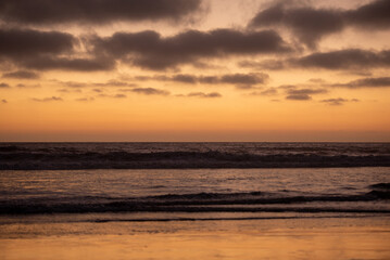 waves crash in pacific ocean with beautiful orange sunset with dark clouds © Schaefer Photography