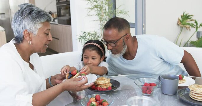 Biracial girl enjoys breakfast with her grandparents, a biracial woman and man