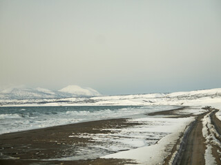 Driving by Northern sea black sand coast in winter, Hitokappu or Kasatka bay on Iturup, Stokap volcano in background, Kuril islands