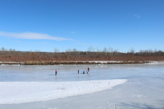 Familia de 5 personas jugando hockey sobre rio congelado con cielo azul de fondo. 