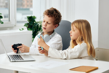 Fototapeta premium Happy Caucasian boy and girl studying together at home using their laptops and headphones for online elearning They are sitting at a table in their living room, fully concentrated on their studies The