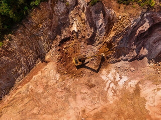 Excavator aerial view. A large yellow crawler excavator moving stone or soil in a quarry. Top view of an excavator digging soil in a construction area. 