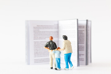 World Book Day concept, Miniature people Happy family reading a book against a white background
