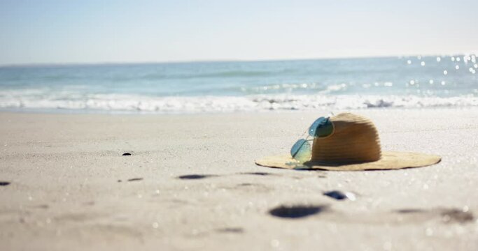 A straw hat and sunglasses rest on a sunny beach with copy space