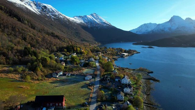 Aerial forwarding shot inside a Norwegian Fjord with a small traditional settlement and snow capped mountains