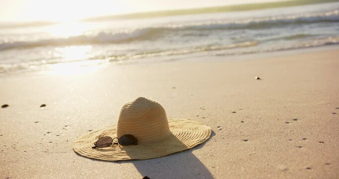 A straw hat and sunglasses rest on a sandy beach, bathed in sunlight, with copy space