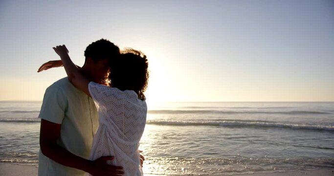 Biracial couple embraces lovingly on a beach at sunset with copy space