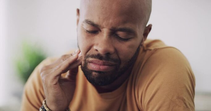 Mouth, toothache or cavity with black man in pain, agony or discomfort in home living room closeup. Dental, gingivitis or tooth decay with person rubbing his cheek or jaw for oral care in apartment