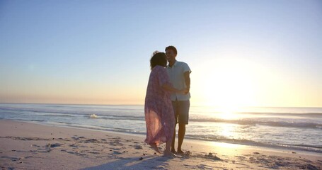 Biracial couple enjoys a playful walk on the beach at sunset