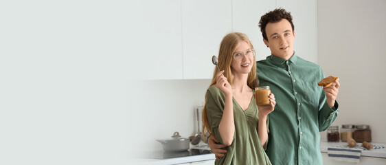 Young woman holding jar of nut butter and handsome man with toast in kitchen