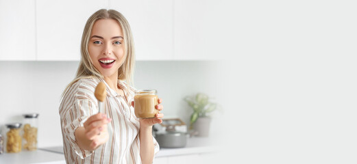Young woman with spoon and jar of nut butter in kitchen