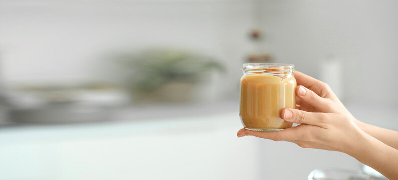 Young woman with jar of nut butter in kitchen, closeup