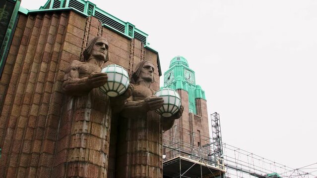 Art deco statues holding lamps at Helsinki Central Station, cloudy sky backdrop
