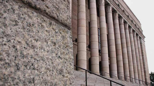 Angled view of the grand Helsinki Parliament House facade, imposing columns, overcast sky