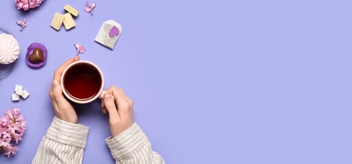 Female hands with cup of hot tea with sweets and flowers on lilac background with space for text - Powered by Adobe