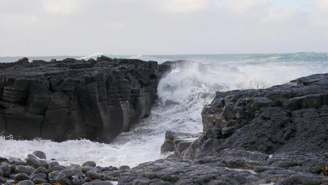 Waves crashing on Iceland's black basalt rock coast, cloudy sky, dynamic ocean scene