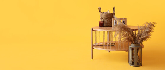 Wooden coffee table with cube calendar, wicker basket and candle holder on yellow background
