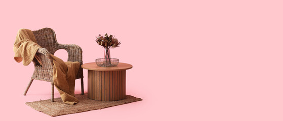 Coffee table with dried flowers in vase near cozy armchair on pink background