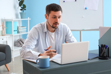 Male tutor with laptop giving online lesson at home