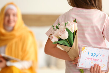 Little girl with greeting card for Mother's Day and tulips in bedroom, back view