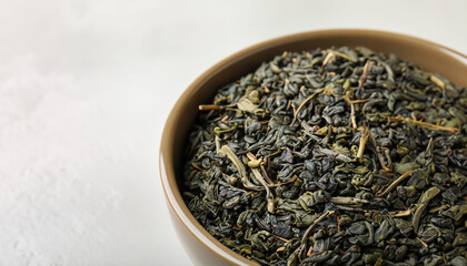 Bowl of dry green tea leaves on light background, closeup view with space for text