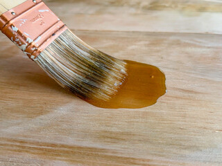 Close-up shot of a paintbrush brushing in polyurethane on a wood plank