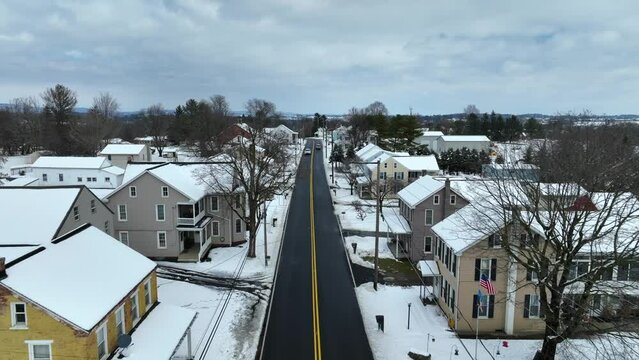 Snow covered homes in american suburb town in winter snow. Car driving on road. Aerial Birds Eye shot. Establishing shot.