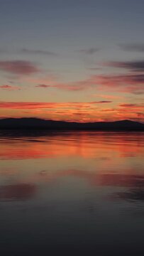 The landscape of an autumn sunset on a lake with calm water. A mirror image of the sky on the water. The natural landscape. Vertical video for shorts.