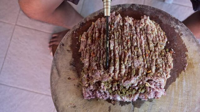a Person is do Chopping Raw Pork Meat with Blakas, a Traditional Balinese Knife on the Wooden Board with top view