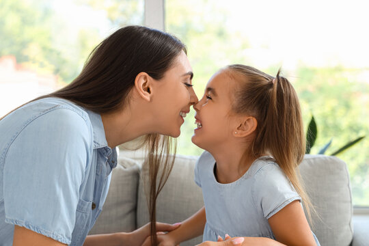 Happy mother with her daughter sitting on sofa in living room and touching noses