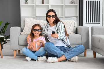 Happy mother and her little daughter in 3D cinema glasses with popcorn watching movie at home