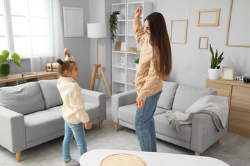 Happy mother with her little daughter dancing in living room at home