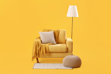 Cozy armchair with cushion, warm blanket and standard lamp on yellow background