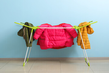 Clean puffer jackets hanging on dryer near blue wall