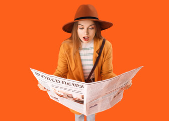 Shocked young woman with newspaper on orange background