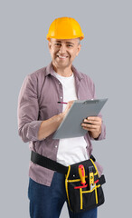 Male construction worker with measuring tape and clipboard on grey background