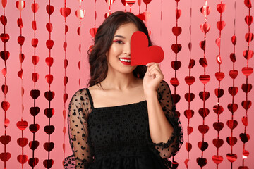 Beautiful young Asian woman with paper heart and hearts-shaped garland on pink background. Valentine's Day celebration