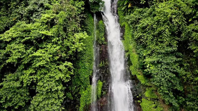 Drone shot, The image captures a verdant waterfall surrounded by lush green foliage, taken from a high vantage point that