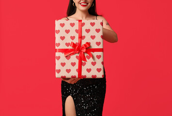 Beautiful young happy woman with gift box on red background. Valentine's Day celebration