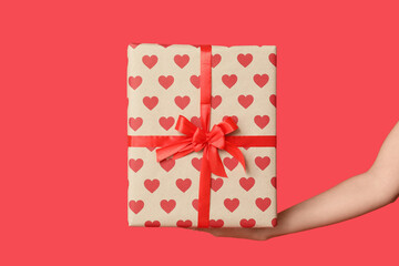 Female hand with gift box on red background. Valentine's Day celebration