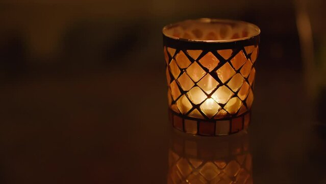 A single glass candle with diamond lattice pattern glows gently in the dark, creating a warm intimate atmosphere. Static shot.