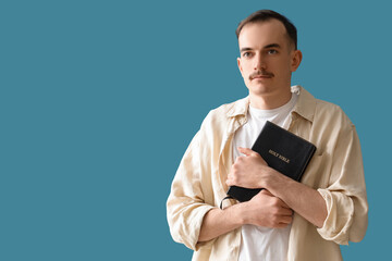Young man with Holy Bible praying on blue background